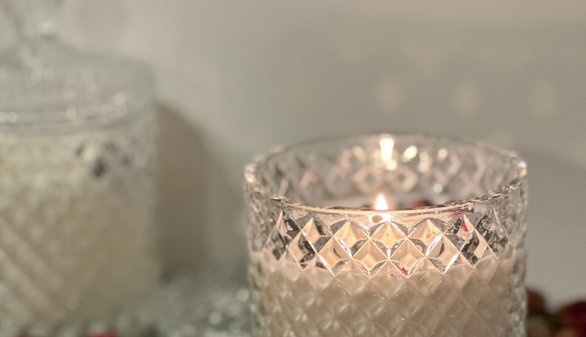 A lit candle in a cut-crystal glass surrounded by dried rosebuds
