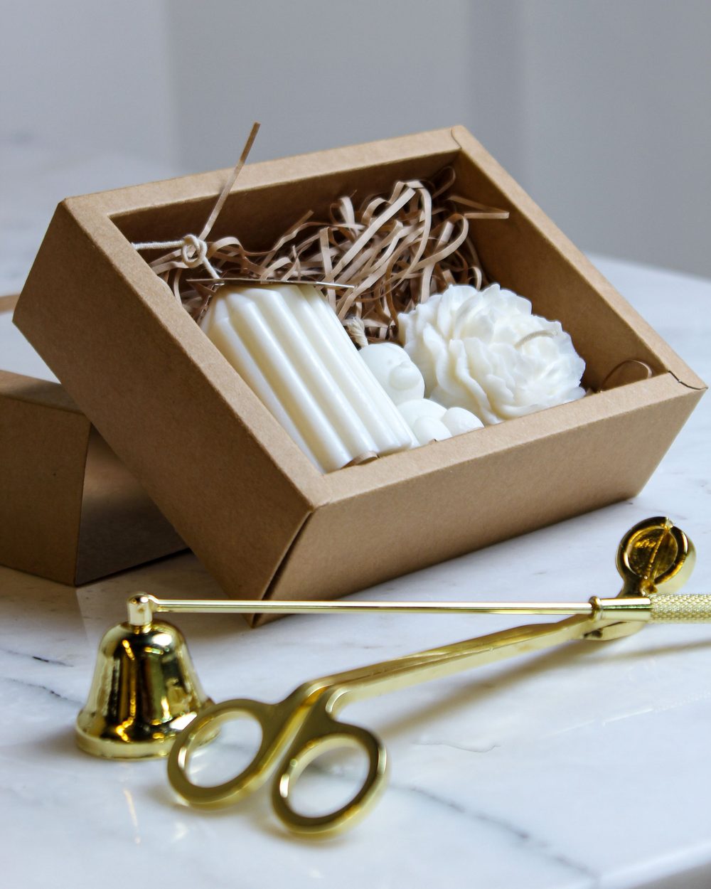 White candles in a gift box with a gold snuffer and wick trimmer