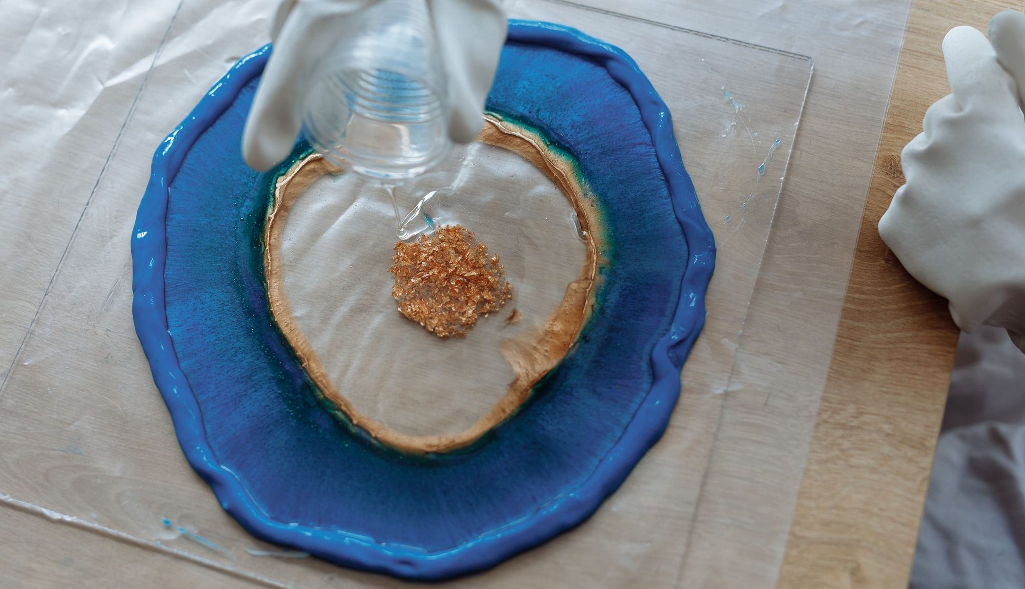 Resin being poured over a blue piece with a gold edge and gold flakes